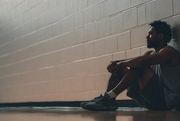 A man in athletic wear sits alone against a gym wall, illustrating the question: do I need therapy.
