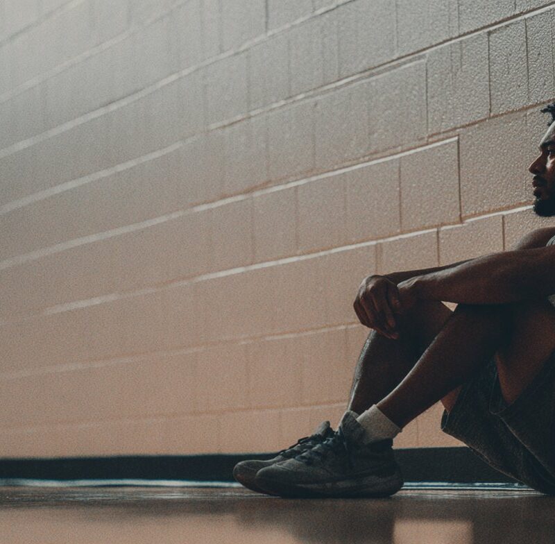 A man in athletic wear sits alone against a gym wall, illustrating the question: do I need therapy.