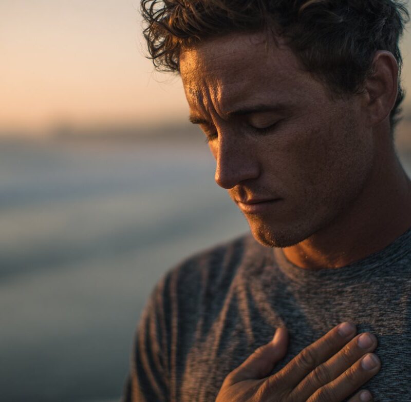 A man holds his hand over his heart at sunset, eyes closed, symbolizing emotional awareness and healing from fawning because trauma.