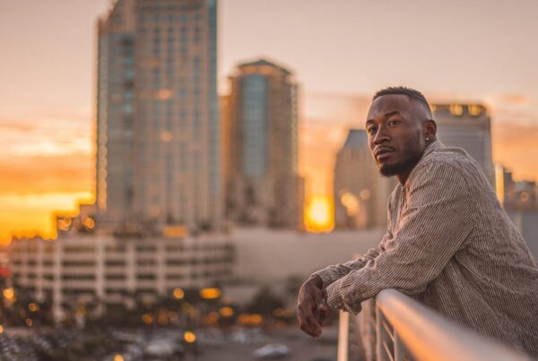 A man leaning on a railing at sunset in a city skyline, appearing deep in thought as the stages of anxiety shift beneath the surface.
