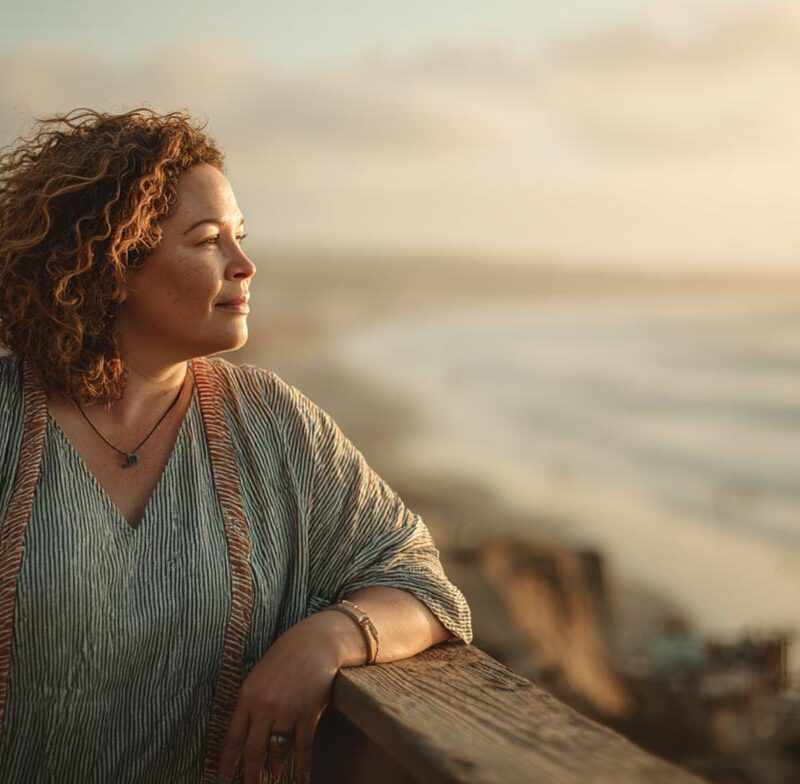 A woman stands alone overlooking the ocean at sunset, reflecting a moment of clarity often reached after recognizing emotional manipulation.