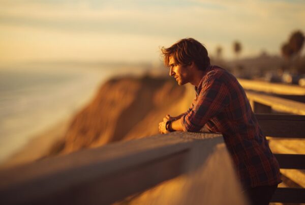 A man leaning on a coastal overlook at sunset deep in thought about his life and emotions, reflecting the question why do I feel empty.